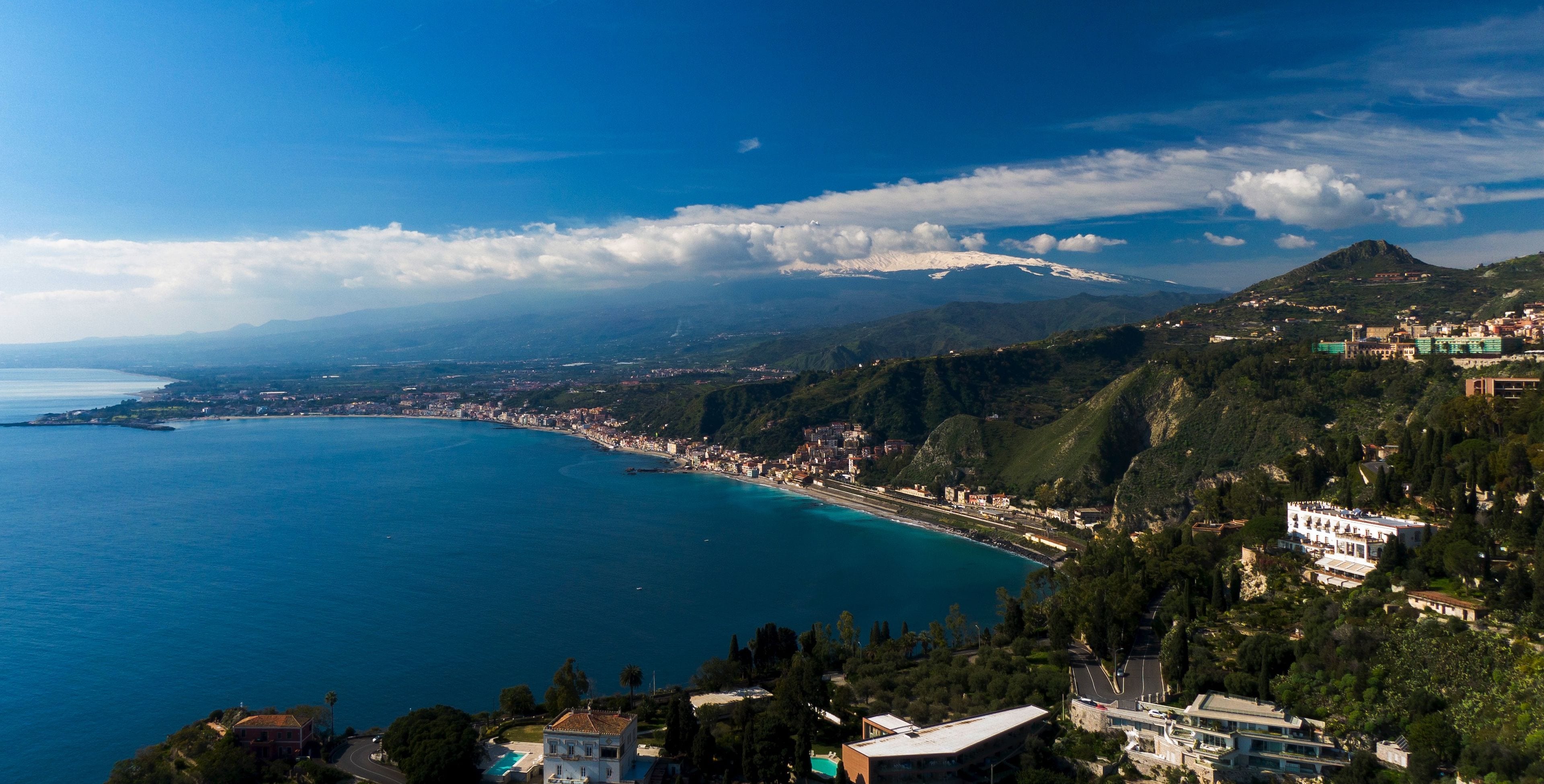 Una località costiera con una montagna sullo sfondo, una spiaggia e degli edifici lungo la costa.