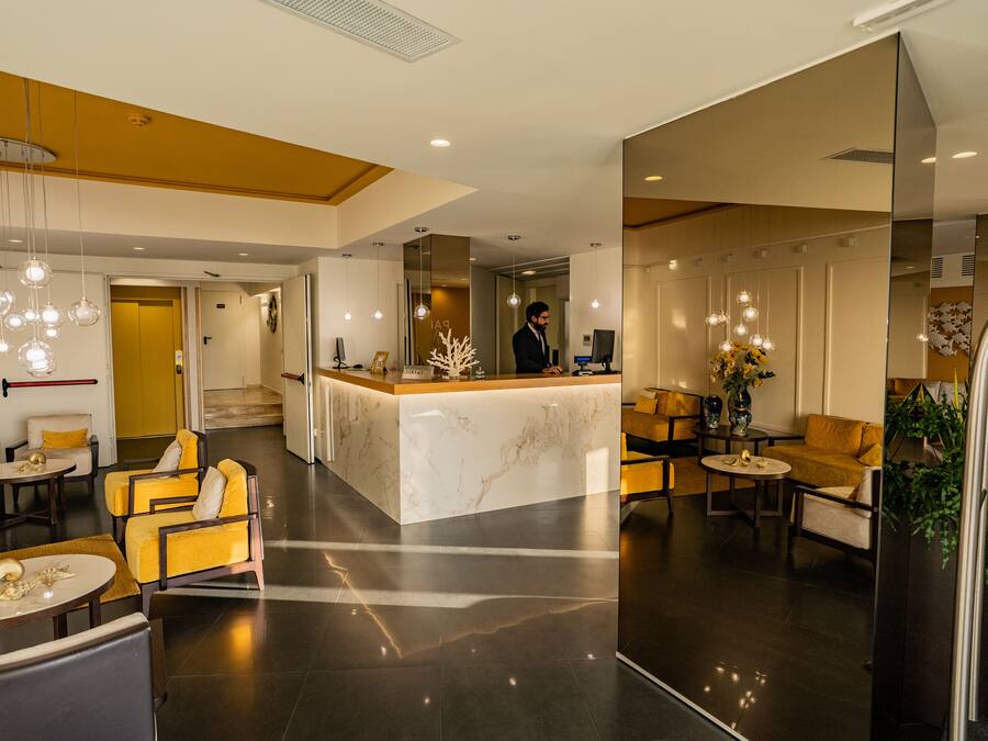 A modern hotel lobby with a marble reception desk, yellow seating, and pendant lighting.
