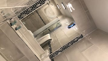 A bathroom with a large mirror, a shower, and a toilet.