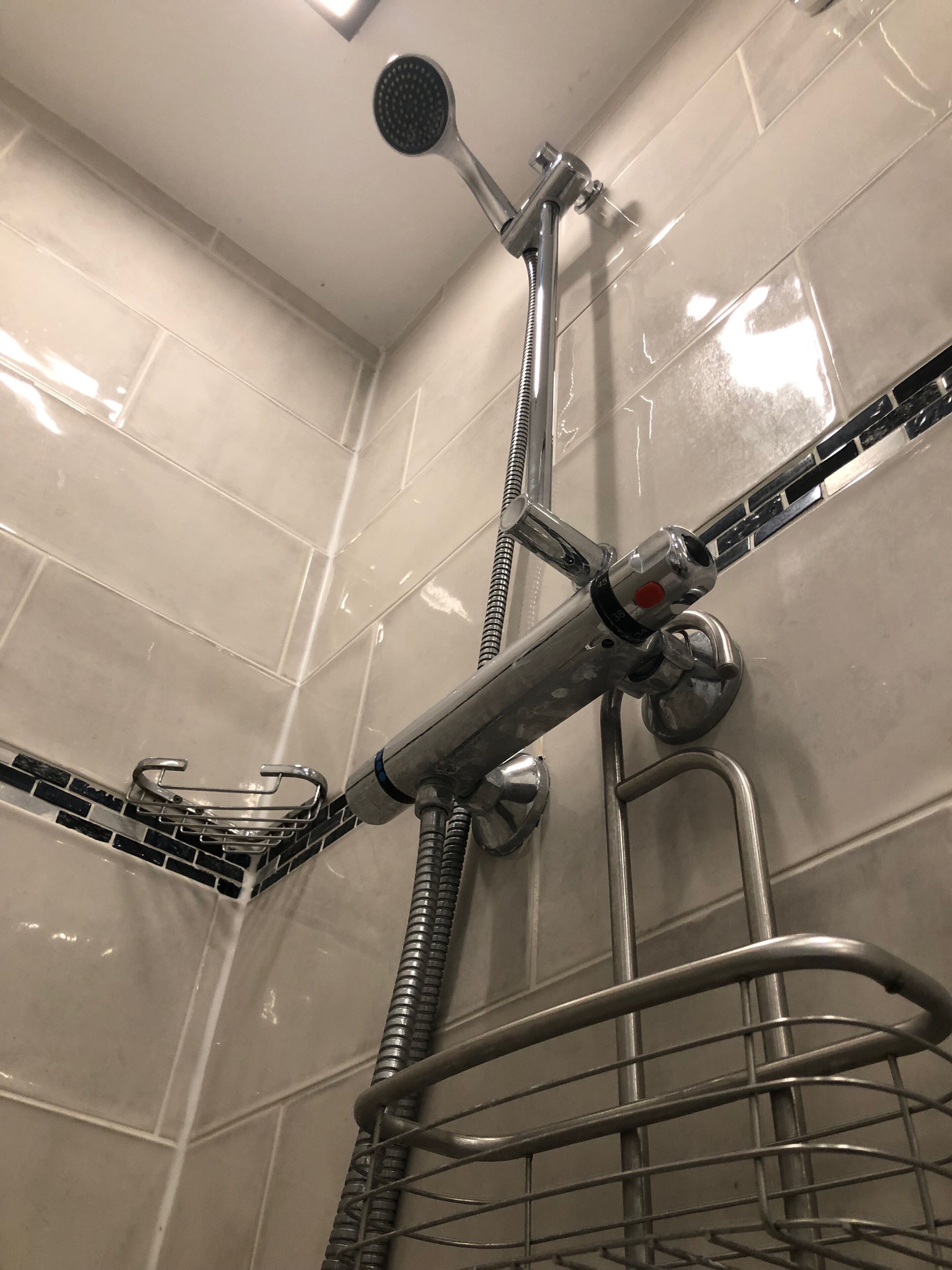 A bathroom with a shower, a metal rack, and tiled walls.