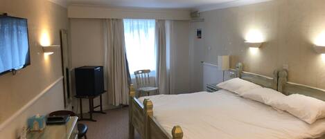 Una camera d'albergo con un letto, una scrivania con una sedia, una televisione e una finestra con tende.