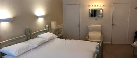 A hotel room with a bed, bedside tables, a chair, a mirror, and a door.