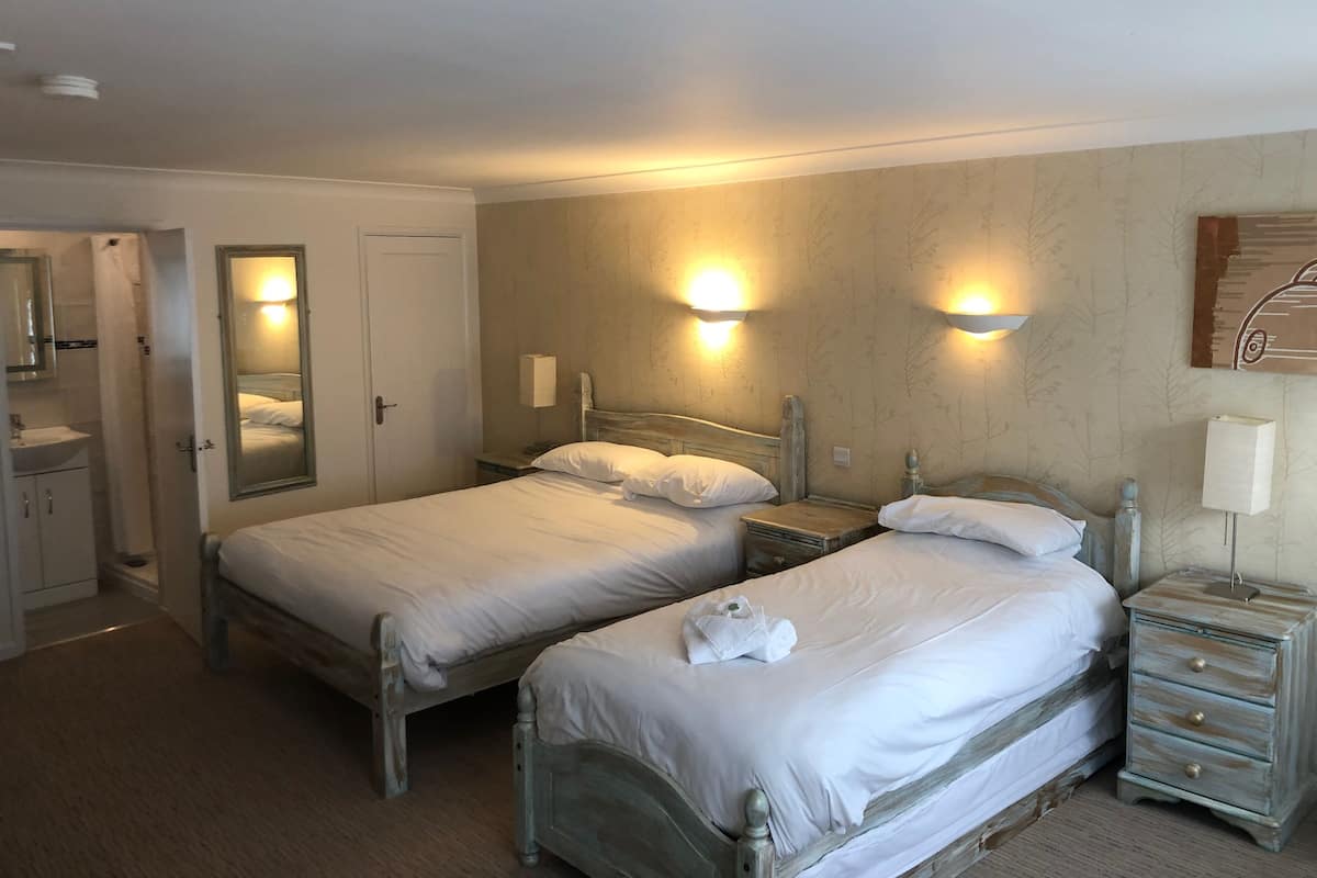 A hotel room with two beds, a bathroom, and a nightstand with a lamp.