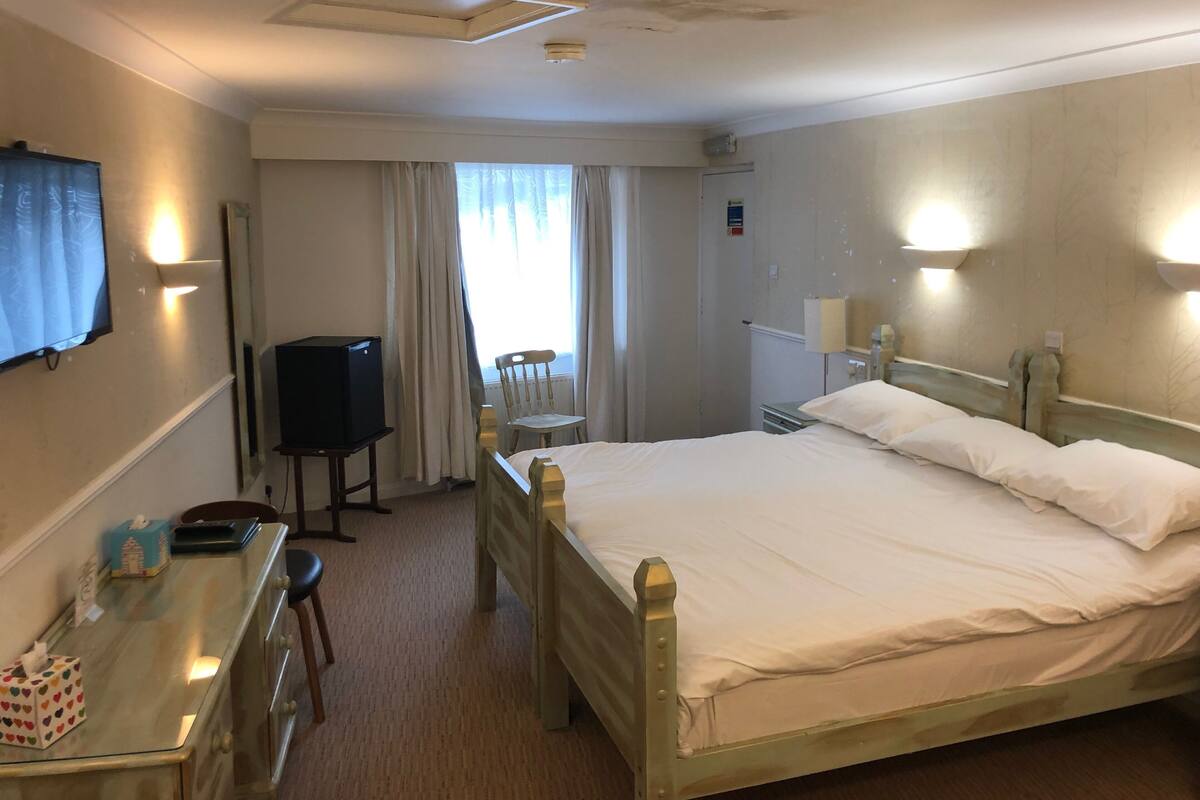 A hotel room with a bed, a desk with a chair, a television, and a window with curtains.