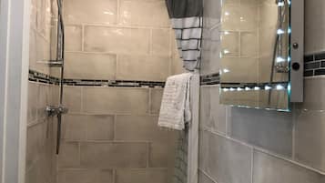 Un baño moderno con cabina de ducha de vidrio, un lavamanos blanco y un espejo con iluminación.