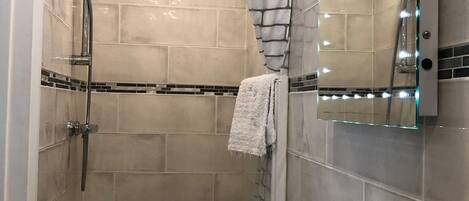 A modern bathroom with a glass shower enclosure, a white sink, and a mirror with lights.