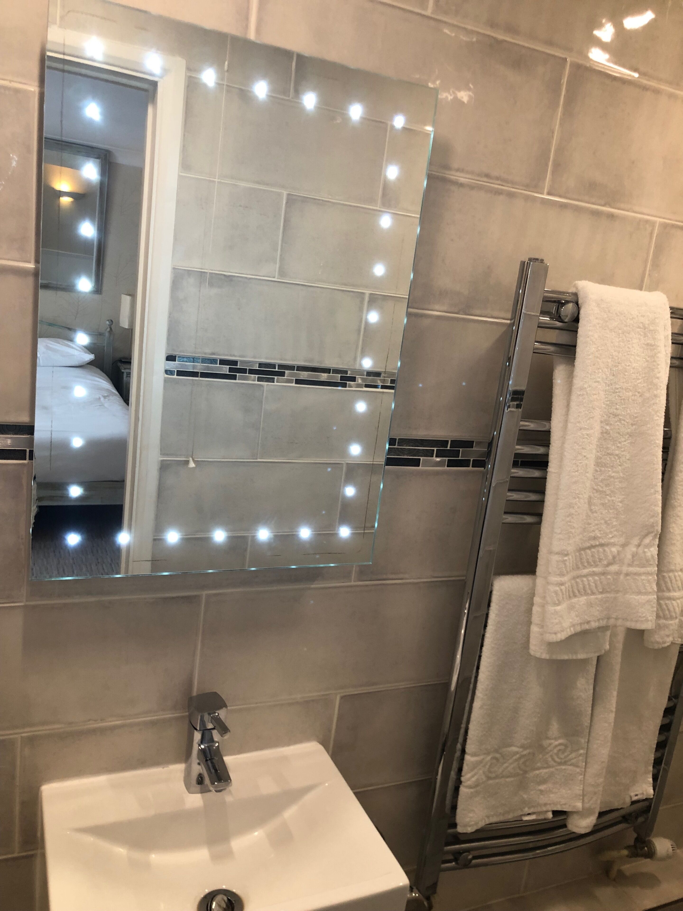 A bathroom with a vanity, a mirror with lights, a towel rack, and a shower.