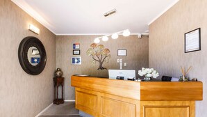 A reception area with a wooden counter, a wall-mounted mirror, framed certificates, and a decorative tree sculpture. - Kauri Court Motel and Apartments (Palmerston North)