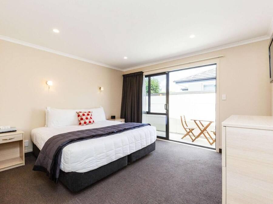 A hotel room with a bed, a nightstand, a TV, and a sliding glass door leading to a balcony.