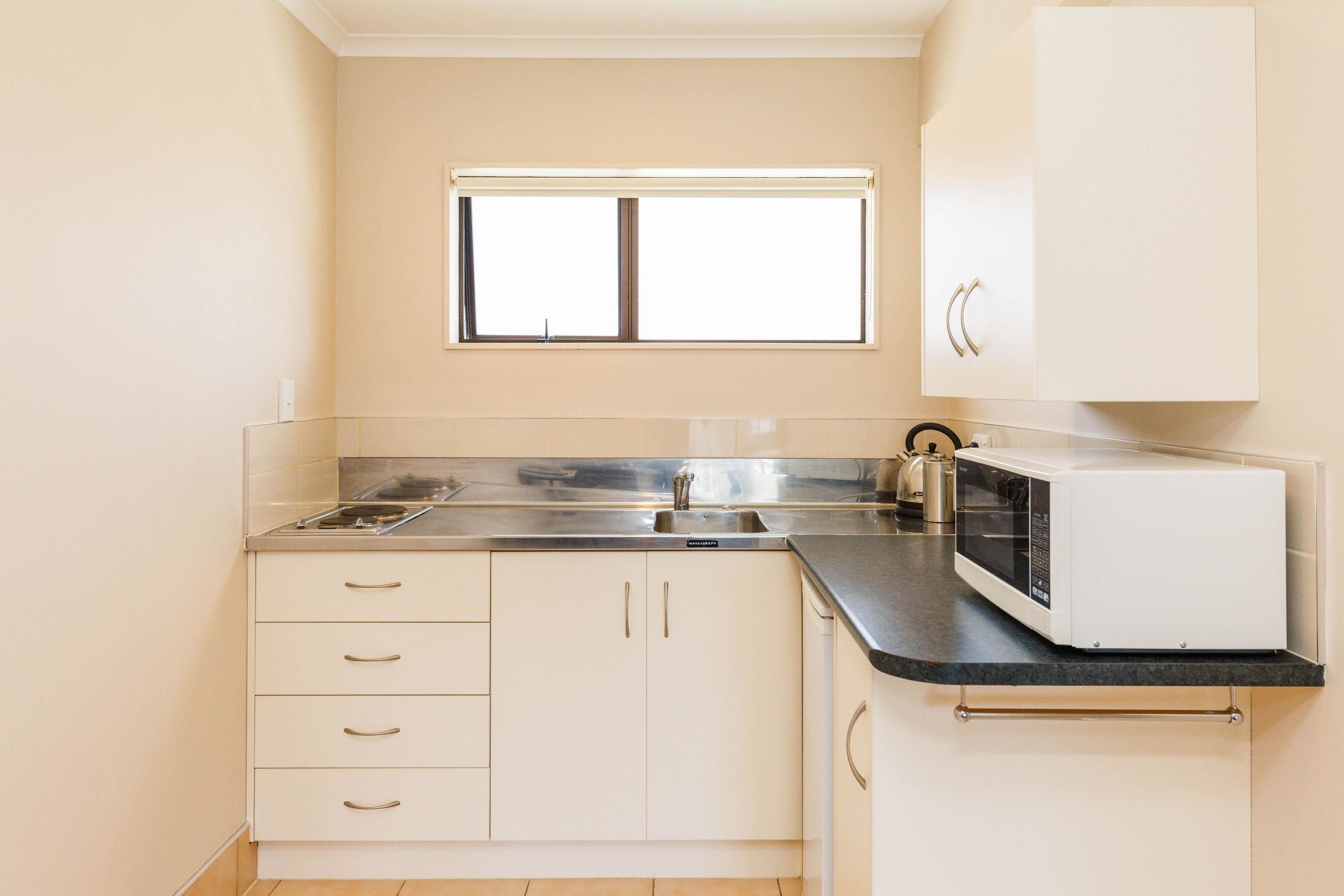 A kitchen with white cabinets, a stainless steel sink, a microwave, and a window above the sink.