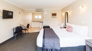 A hotel room with a bed, desk, chair, and kitchenette in the background. - Kauri Court Motel and Apartments (Palmerston North)