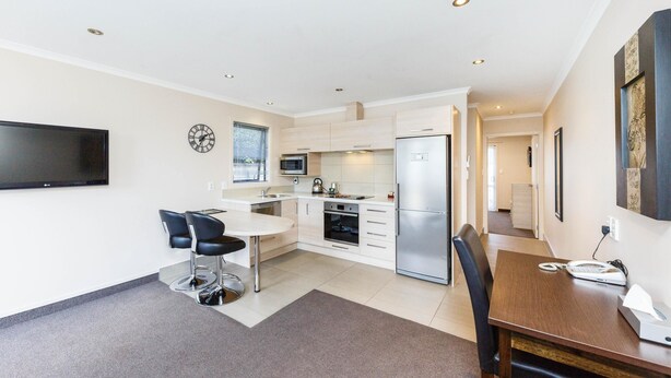 A modern kitchen with white cabinets, a stainless steel refrigerator, and a dining area with a table and chairs. - Kauri Court Motel and Apartments (Palmerston North)