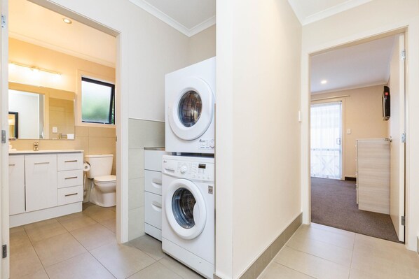 A modern bathroom with a toilet, sink, and stacked washing machine. - Kauri Court Motel and Apartments (Palmerston North)
