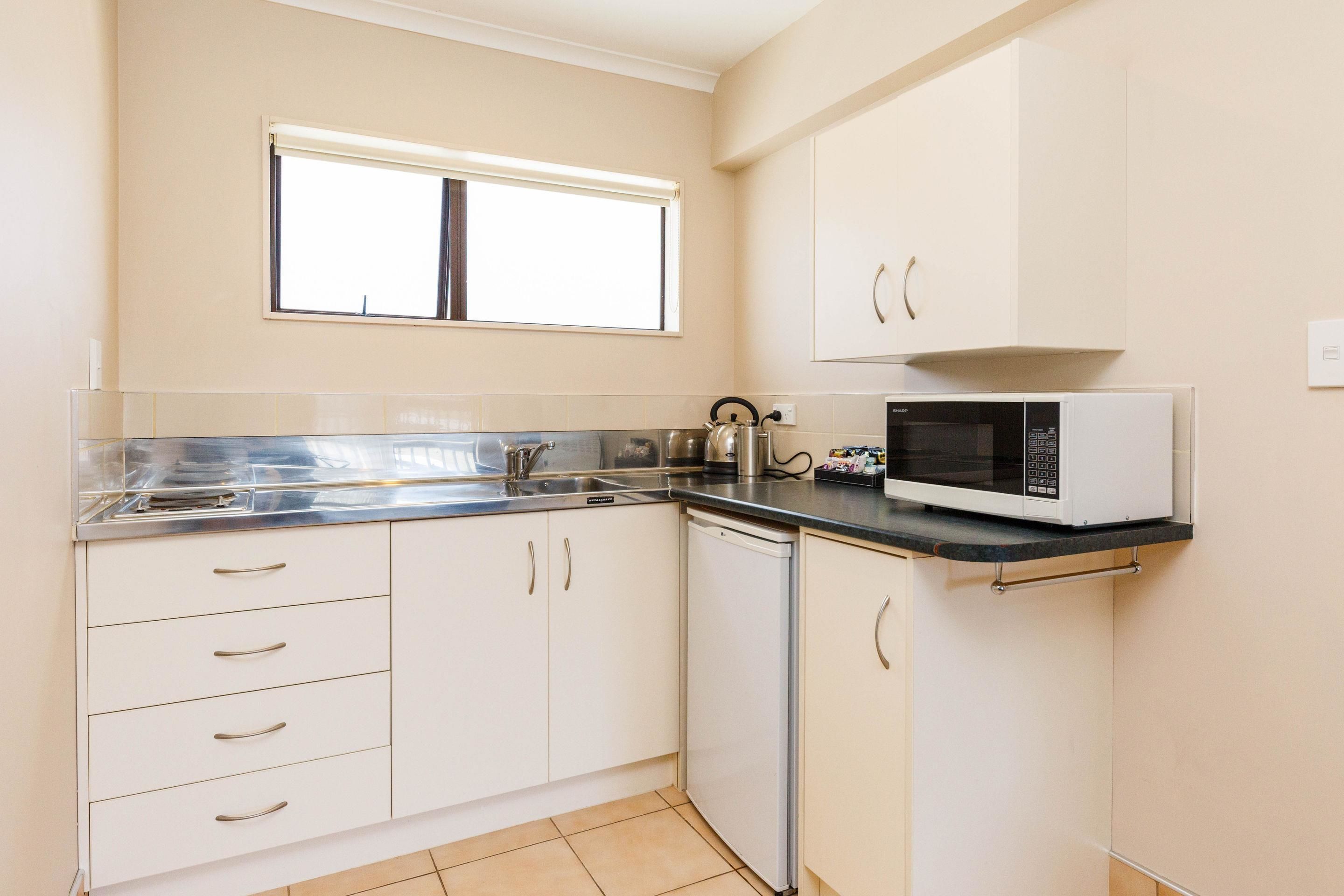 A kitchen with white cabinets, a microwave, a kettle, and a window above the sink.