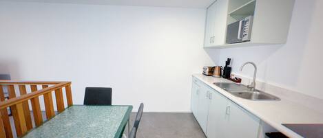 Una cocina compacta con una mesa, una silla, un microondas y un lavamanos.