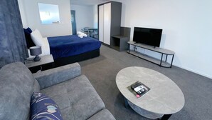 A modern hotel room with a bed, a TV, a sofa, and a small table. - Brylin Motel (Rotorua)