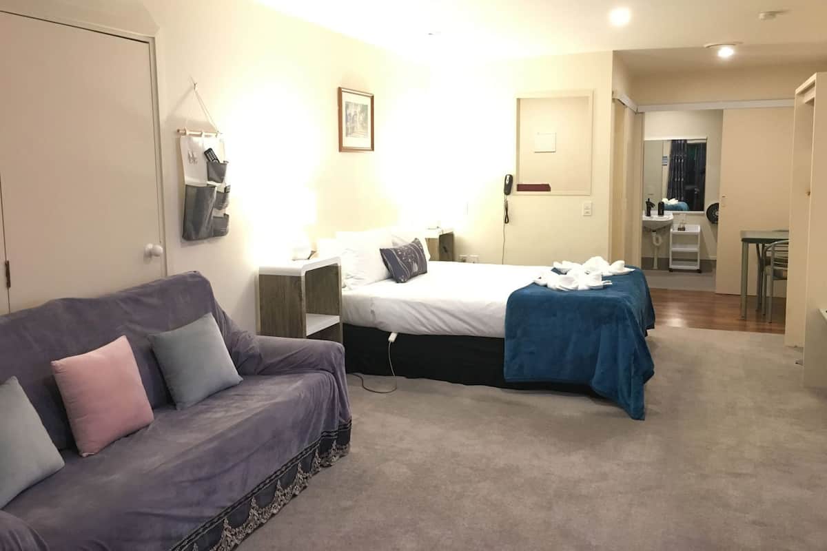 A bedroom with a bed, a sofa, a desk, a mirror, and a bathroom visible through an open door.