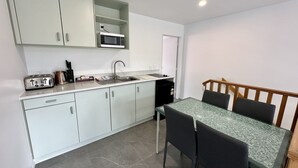A compact kitchen with white cabinets, a microwave, a sink, and a small dining area with a table and chairs. - Brylin Motel (Rotorua)