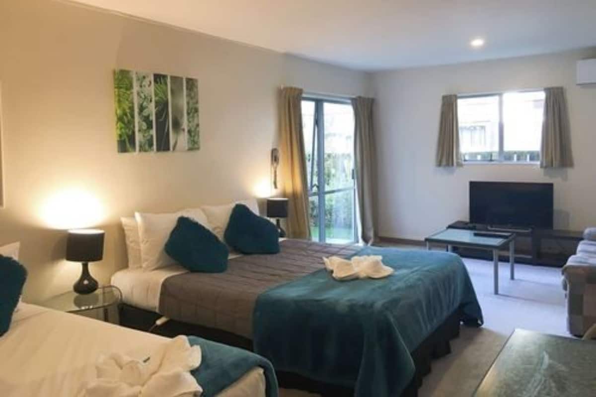 A hotel room with two beds, a TV, a desk, and a balcony.
