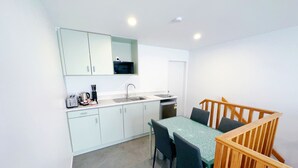 A compact kitchen with a sink, a small refrigerator, and a microwave. There is a dining table with four chairs and a wooden railing. - Brylin Motel (Rotorua)