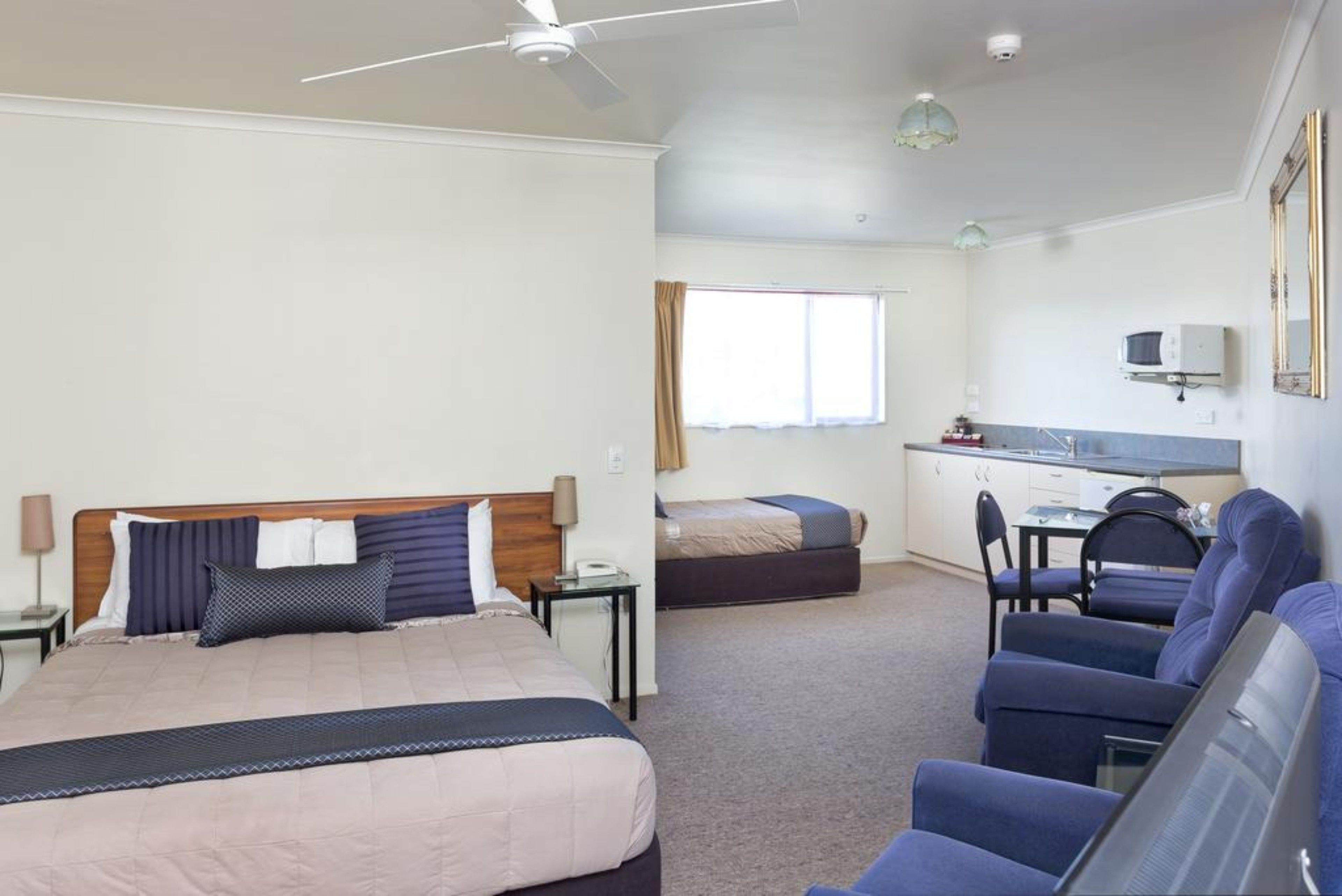 A hotel room with a bed, a desk, a chair, and a kitchenette.
