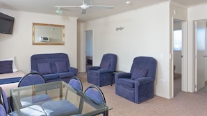 A room with a glass table, two blue sofas, a single armchair, and a ceiling fan. - BK's Rotorua Motor Lodge (Rotorua)