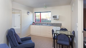 A compact kitchen with a window, a microwave, and a dining area with chairs. - BK's Rotorua Motor Lodge (Rotorua)