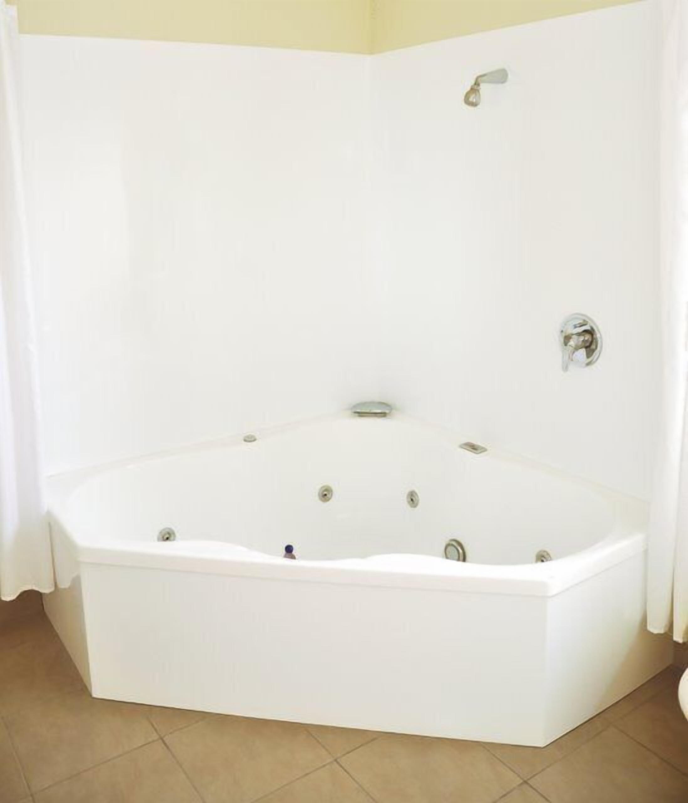 A corner bathtub with a showerhead and controls, tiled floor, and a curtain.