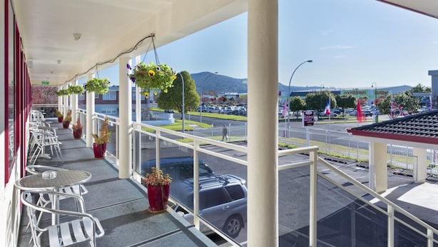 A covered outdoor seating area with metal chairs and tables, potted plants, and a view of a parking lot and distant mountains. - BK's Rotorua Motor Lodge (Rotorua)