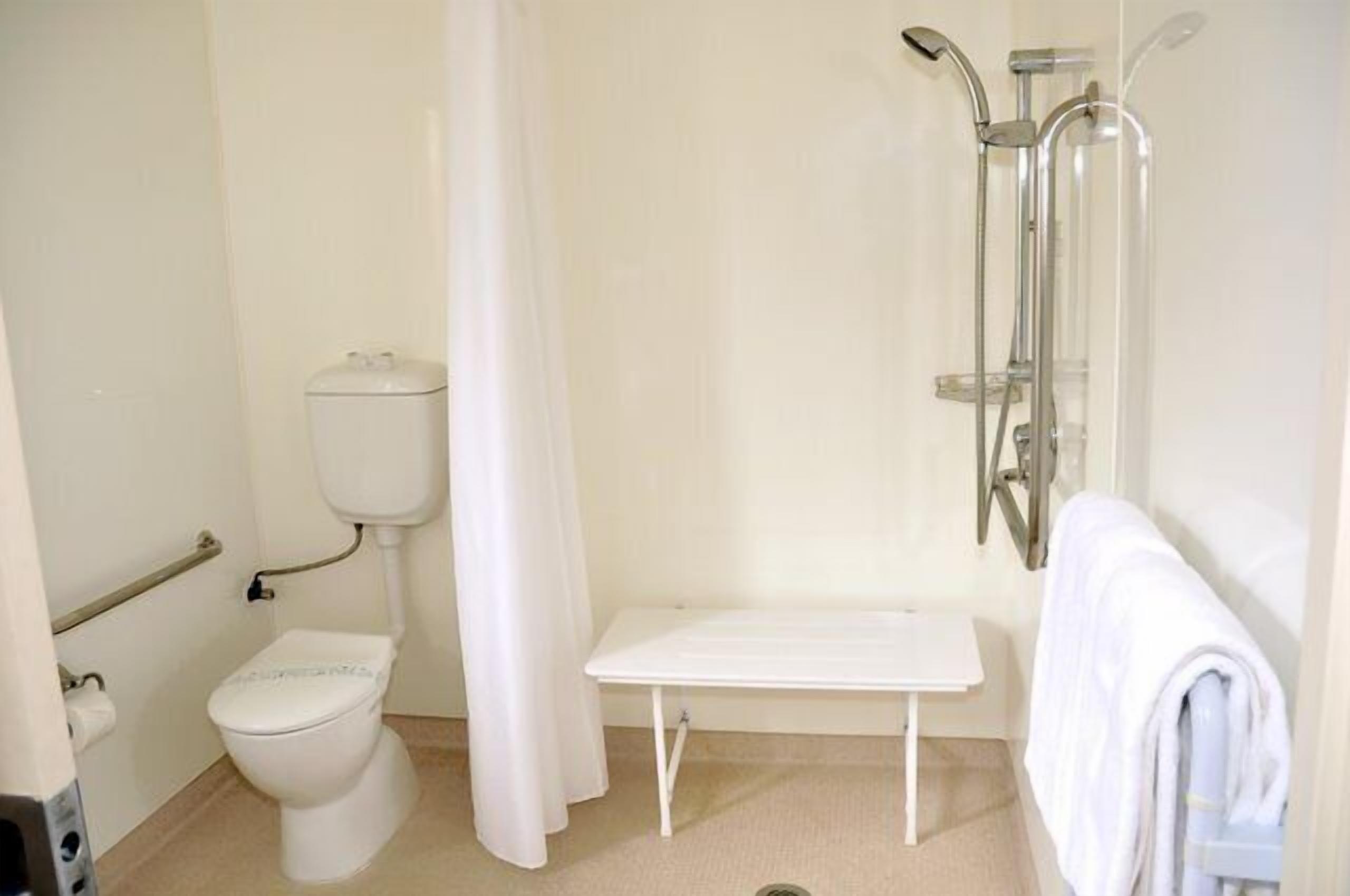 Ein kleines, sauberes Badezimmer mit Toilette, Dusche und Sitzbank.
