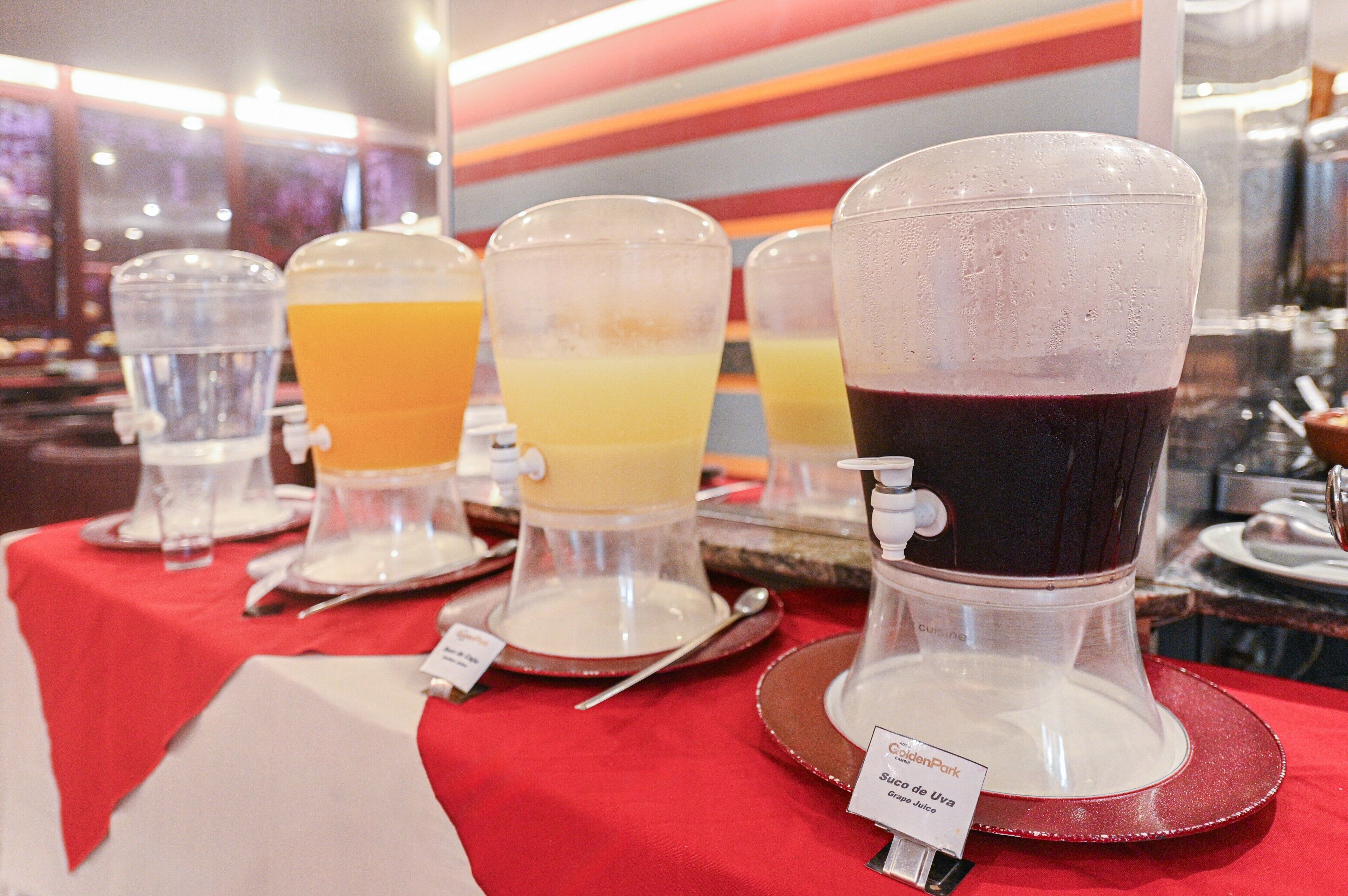 A buffet with various beverages in dispensers, including a dark red drink, a yellow drink, and a clear drink.