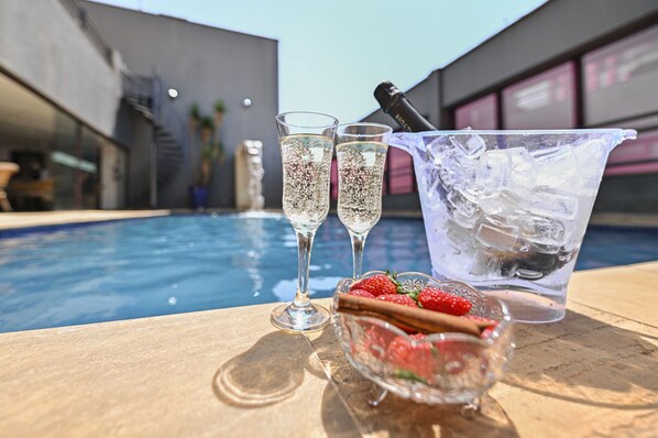 Escena junto a la piscina con dos copas de champán, un balde de hielo y un bol con fresas y palitos de canela.
