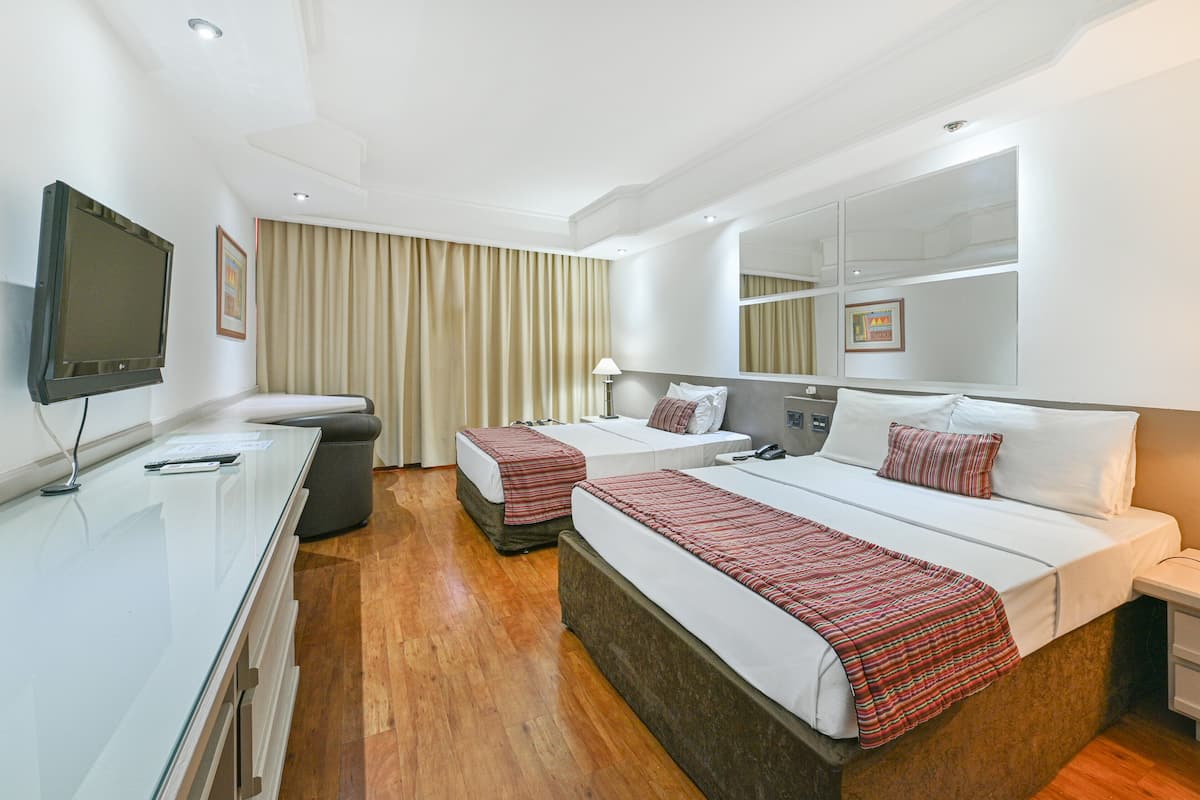 Una habitación de hotel con dos camas, televisión, escritorio y espejo.