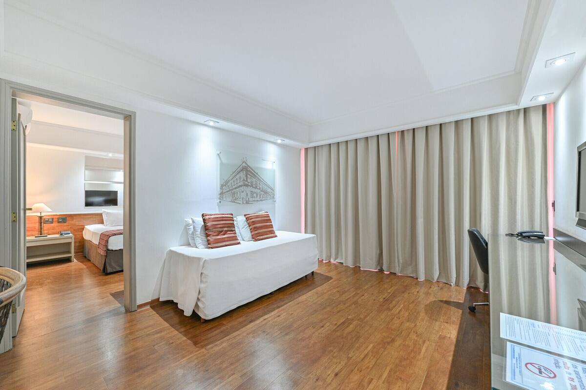 Una habitación de hotel con cama, escritorio, silla, televisor y cortina.