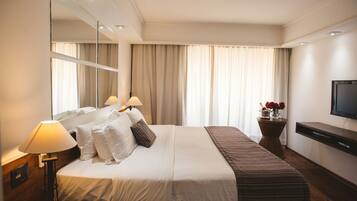 Une chambre d’hôtel avec un lit, des lampes de chevet, une télévision, un miroir et une fenêtre avec des rideaux.