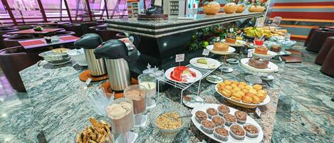A buffet with various food items, including cakes, muffins, and fruits.