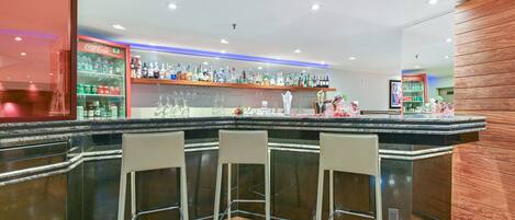 Zona de bar con mostrador, tres taburetes y una variedad de botellas y vasos.