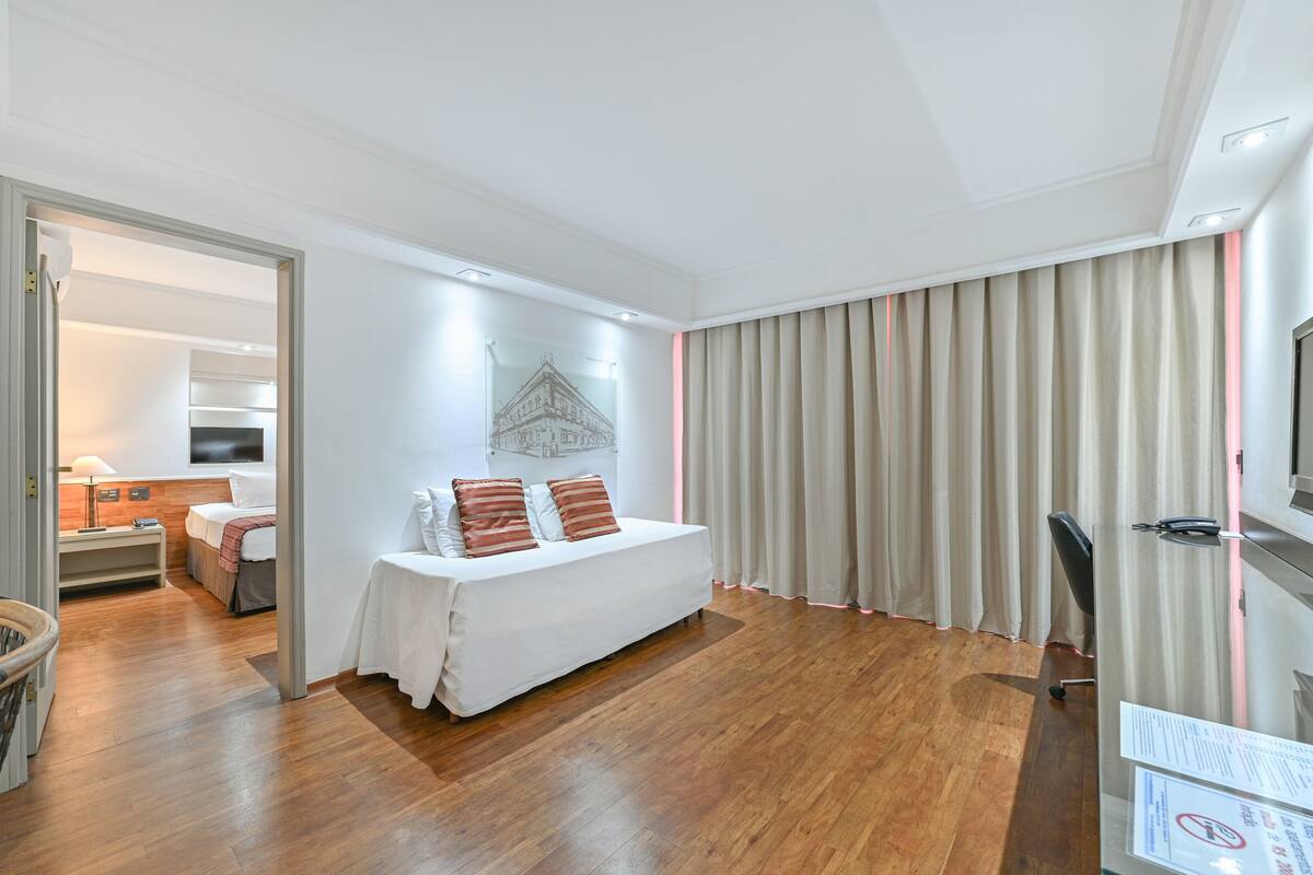 Una habitación de hotel con cama, mesita de noche, lámpara y cortinas.