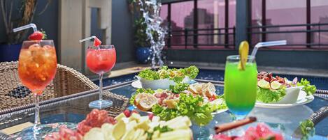 A dining table with various food items and drinks, a water feature, and a view of the city.
