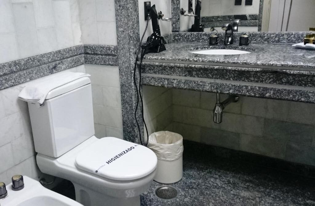 Ein Badezimmer mit Toilette, einem Waschbecken mit Granitplatte, einem Spiegel und einem Mülleimer.