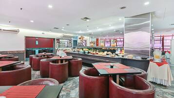Um restaurante com cabines e mesas, um buffet com diversos pratos e um balcão com dispensador de bebidas.