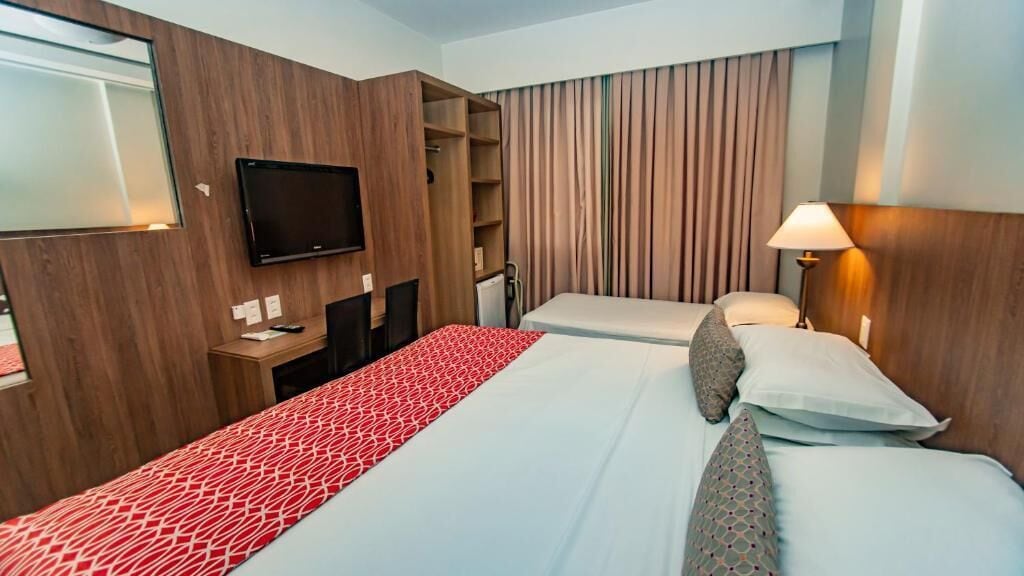 A hotel room with a bed, a TV mounted on the wall, a desk, and a wardrobe.