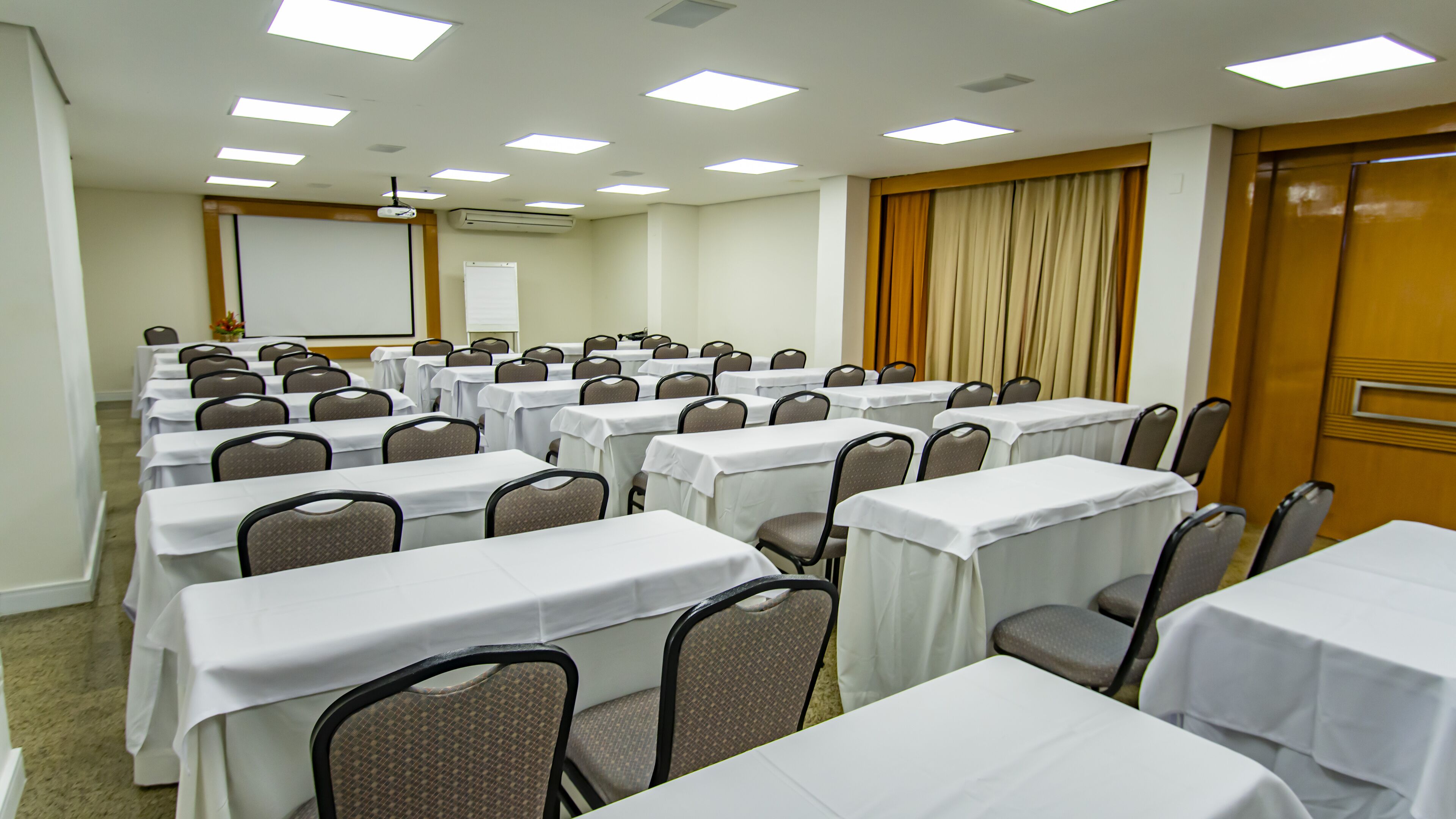 A conference room with rows of tables and chairs, a projector screen, and a whiteboard.