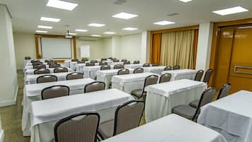 A conference room with rows of tables and chairs, a projector screen, and a whiteboard.