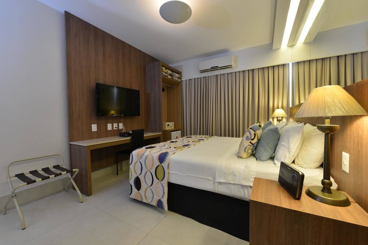 Ein Hotelzimmer mit Bett, Nachttisch, Lampe, Fernseher, Schreibtisch und Kleiderschrank.