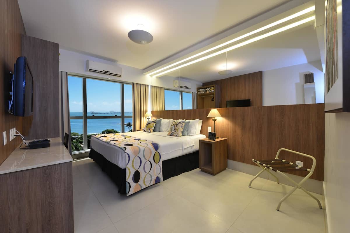 Ein modernes Hotelzimmer mit einem großen Bett, Nachttischlampen, einem Fernseher und Meerblick.