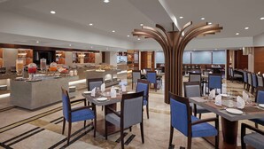 A modern hotel dining area with a buffet, multiple dining tables, and a central decorative wooden structure. - Best Western Plus Indore (Indore)
