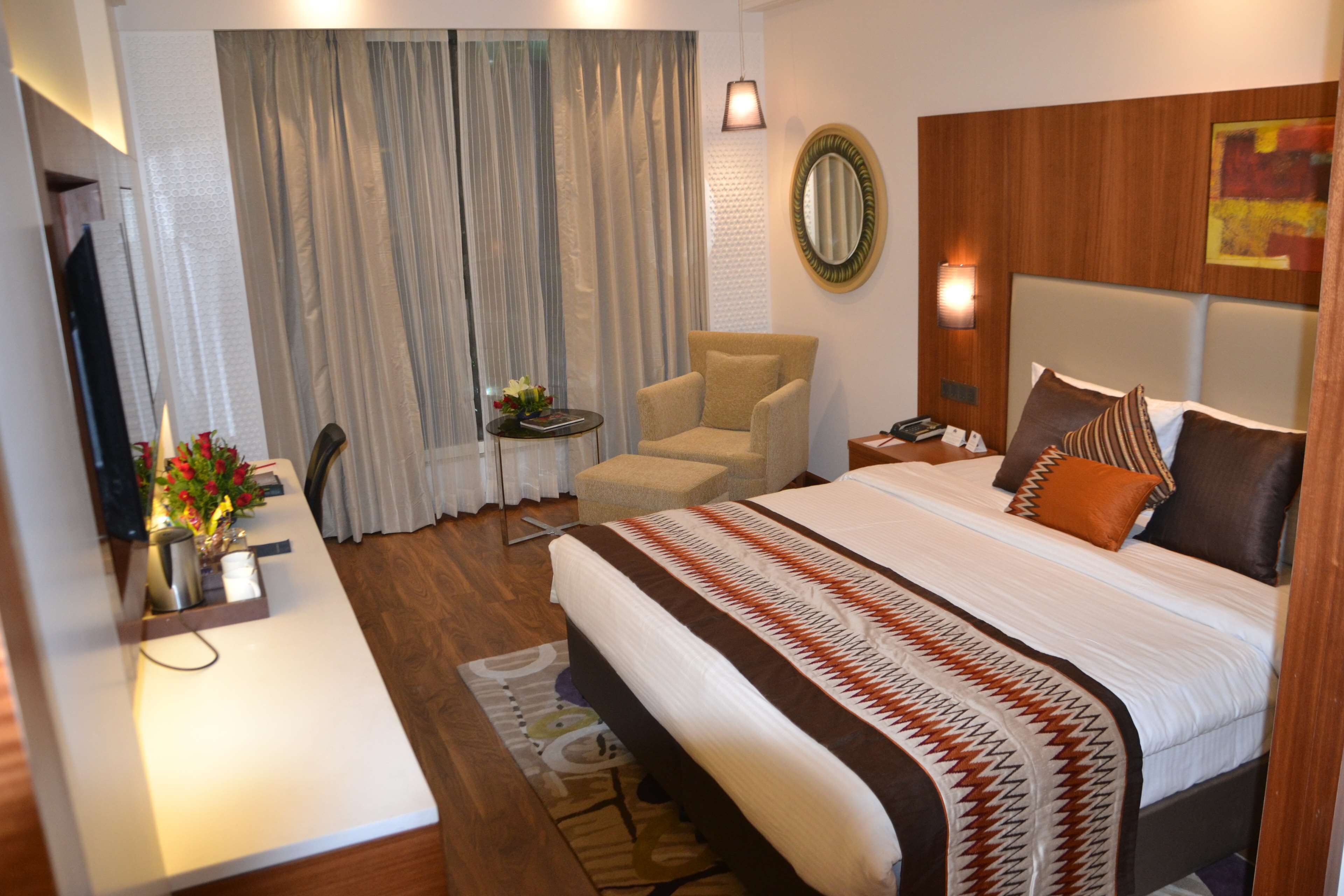 A hotel room with a large bed, a chair, a desk, and a mirror on the wall.
