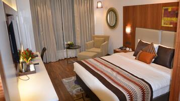 A hotel room with a large bed, a chair, a desk, and a mirror on the wall.