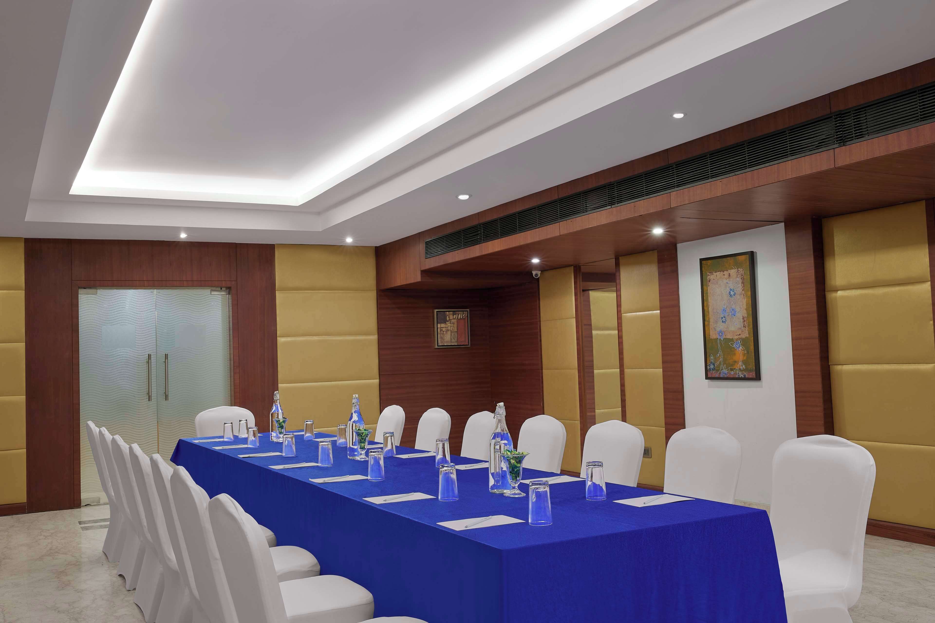 Un salón de conferencias con una mesa larga, sillas blancas y manteles azules.